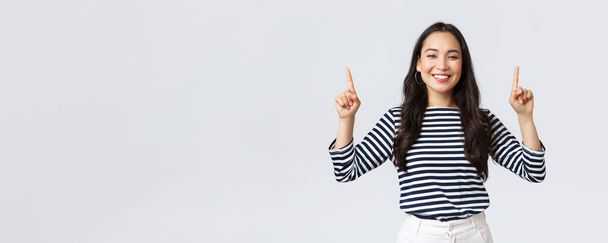 Lifestyle, beauty and fashion, people emotions concept. Cheerful good-looking female model pointing fingers up to shop promotion banner, smiling camera, recommend click link to online store - 写真・画像