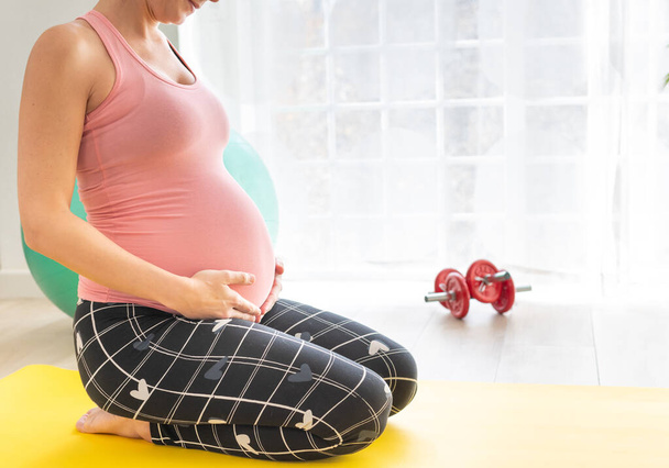 молода вагітна жінка посміхається, коли вона торкається її животик вона на колінах на фітнес-матусі робить вправи і розтягування вагітної жінки посміхається, коли вона торкається її животик вона на колінах на фітнес-матусі робить вправи і розтягується
 - Фото, зображення