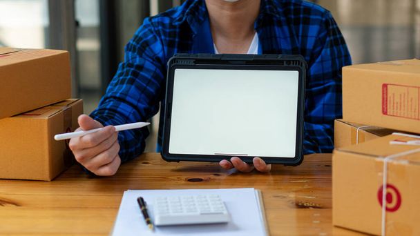 jeune homme tenant un stylo pointant vers une tablette avec un écran blanc et une boîte à côté d'une calculatrice d'idée d'entreprise sme - Photo, image