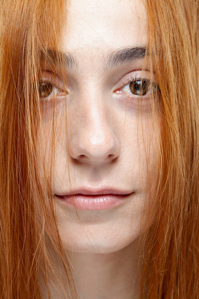 美しい暗い焦げたオレンジの髪の女の子のカメラを見て。灰色の背景に深刻な表情を持つスタジオポートレート. - 写真・画像
