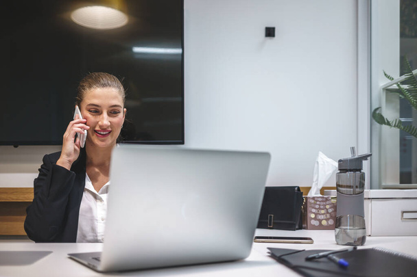 Femme d'affaires souriante parlant sur smartphone dans l'espace de travail - Photo, image