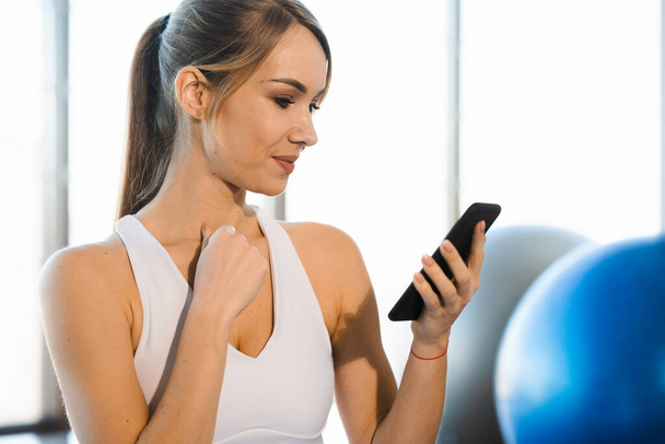 Retrato de cerca de una hermosa chica fitness con un teléfono inteligente en el interior - Foto, Imagen