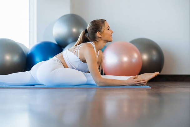 Chica flexible en ropa de yoga blanco practicando twine en gimnasio - Foto, imagen