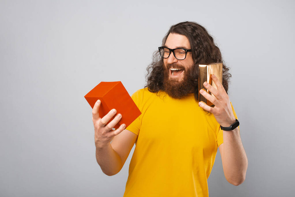 Verbazingwekkende bebaarde hipser man met lang haar op zoek in doos cadeau. - Foto, afbeelding
