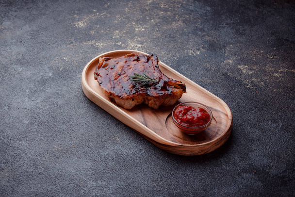 Flat lay of grilled pork steak in caramelized sauce. Serving meat on eco-friendly wooden utensils. A sprig of fresh rosemary and tomato sauce. - Foto, afbeelding