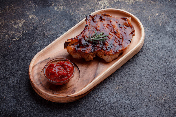 Flat lay of grilled pork steak in caramelized sauce. Serving meat on eco-friendly wooden utensils. A sprig of fresh rosemary and tomato sauce. - Fotó, kép