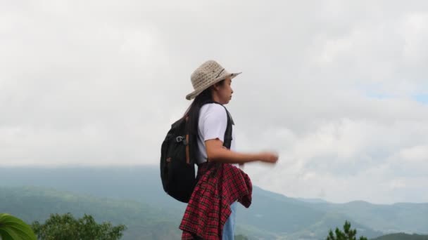 Sırt çantalı bayan yürüyüşçü kollarını kaldırarak dağın tepesinde duruyor ve manzaranın tadını çıkarıyor. yolculuk ve başarı kavramı - Video, Çekim