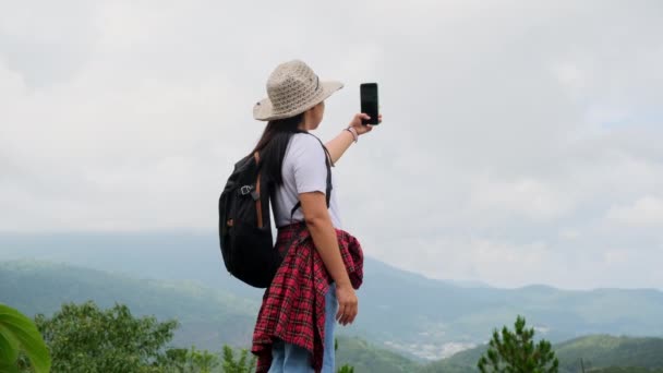 Hipster vrouw in een hoed ontspant in de natuur op vakantie en maakt gebruik van smartphone neemt een selfie op een berg achtergrond. - Video