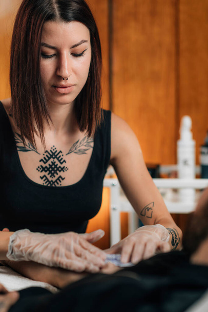 Tatuaje. Artista del tatuaje femenino que aplica la plantilla del tatuaje en el brazo masculino antes de tatuar - Foto, Imagen