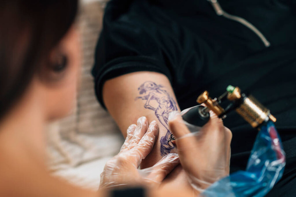 Női tetováló művész tetováló férfi kar a stúdióban  - Fotó, kép