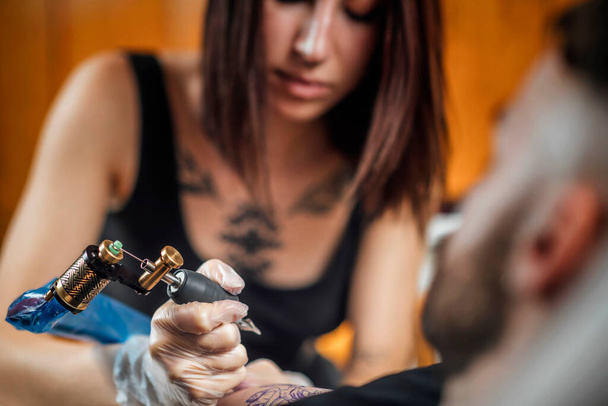 Female tattoo artist tattooing mans arm in studio  - Photo, Image