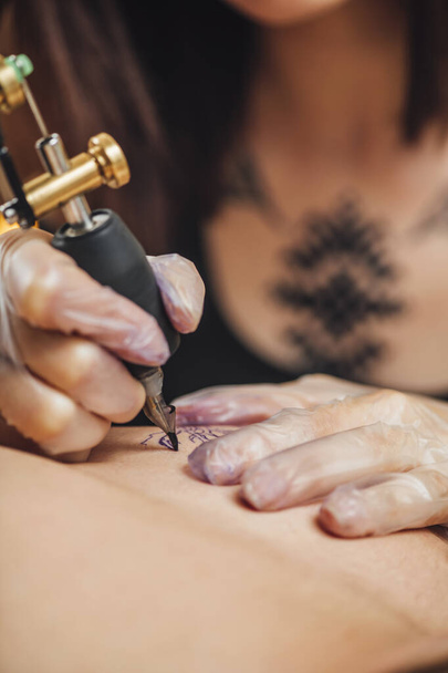 Tetováló keze gumikesztyűben tetoválás elektromos tetoválópisztollyal, közelkép - Fotó, kép
