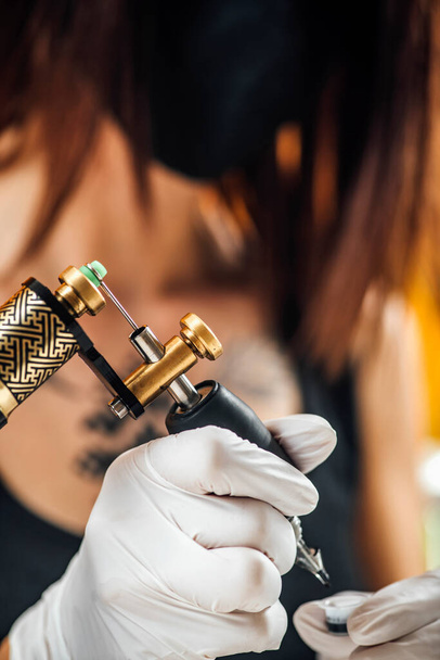 Tatuaje femenino artista prepara máquina de tatuaje para hacer un tatuaje en un brazo de hombre  - Foto, imagen