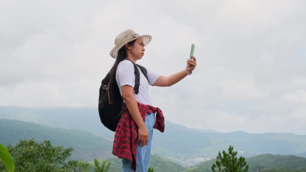 Hipster mujer en un sombrero trata de obtener una señal de un teléfono móvil en las montañas. Senderista en una mochila se para en una montaña tratando de captar una señal de teléfono celular. - Metraje, vídeo