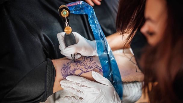Вид сверху на тату-мастера, татуирующего руку в студии  - Фото, изображение