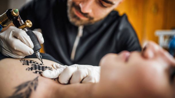 Tatuaje masculino artista tatuando a mujer joven en estudio de tatuaje - Foto, Imagen