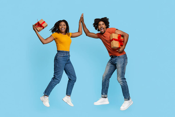 Эмоциональный черный мужчина и женщина с подарками, дающими пять - Фото, изображение