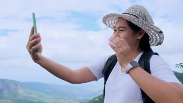 帽子のヒップスター女性は休暇中に自然の中でリラックスし、山の背景にスマートフォンでビデオ通話を行う. - 映像、動画