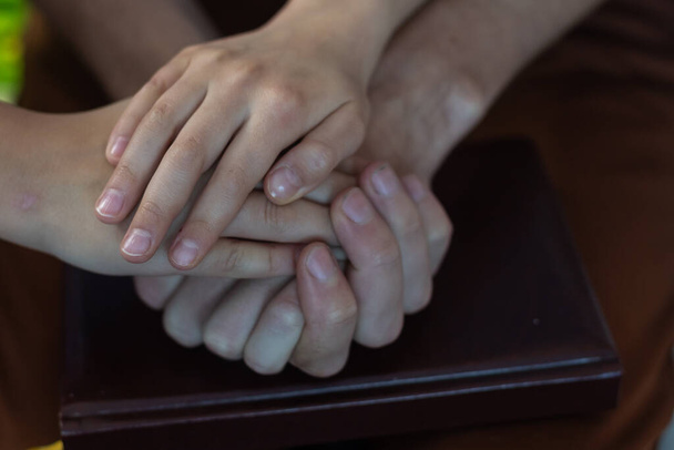 Bovenaanzicht van ouders en kind die lege handen bij elkaar houden aan houten tafel, ruimte voor tekst. Familiedag - Foto, afbeelding