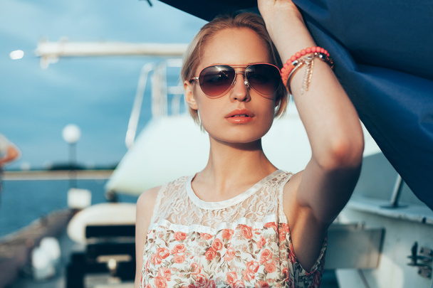Blonde girl in flower dress and sunglasses holding  boat sails - Foto, Imagen