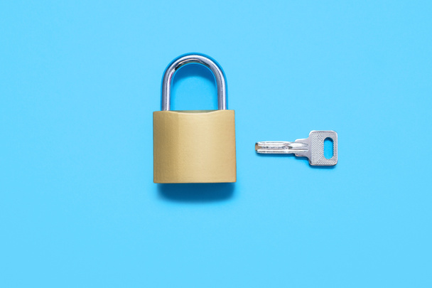 Padlock with a key on a blue background, top view. A gold-colored lock with a silver key on a uniform blue background. The concept of protection and security in the form of a lock and key - Φωτογραφία, εικόνα