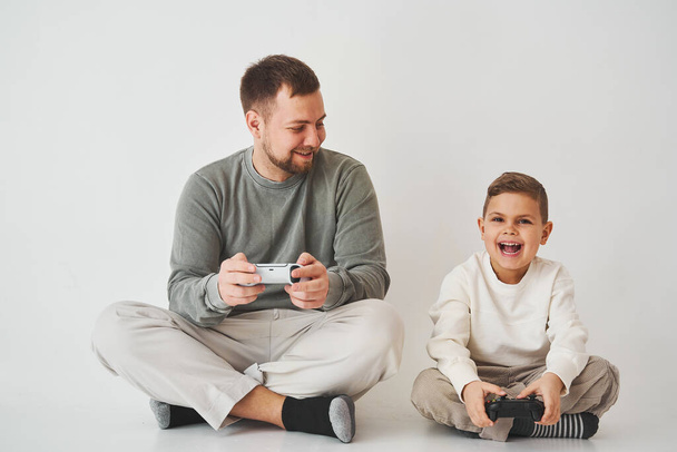 Sohn und Vater spielen Konsolenspiele mit Gamepad. Junge und sein Vater verbringen Zeit miteinander und spielen Computerspiele - Foto, Bild