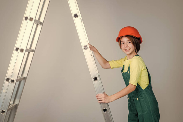 teen girl laborer in protective helmet and uniform on ladder, building - Фото, зображення