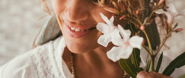 Close-up van vrouw glimlach met witte bloemen op de voorgrond. Banner imago van vrolijke vrouwen. Serene en vreugdevolle uitgebalanceerde lifestyle mensen. Focus op de lippen. Blanke jonge volwassen vrouw - Foto, afbeelding