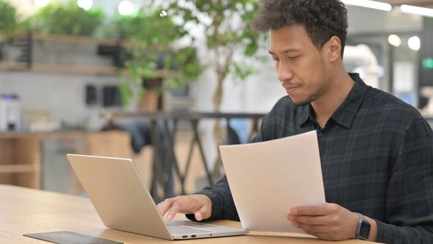 Uomo afroamericano con documenti per la lettura di laptop  - Foto, immagini