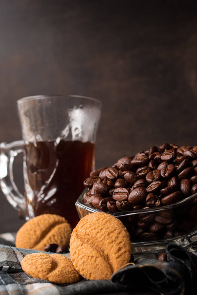 Alguns grãos de café preto em uma panela de vidro ao lado de uma xícara de café preto - Foto, Imagem