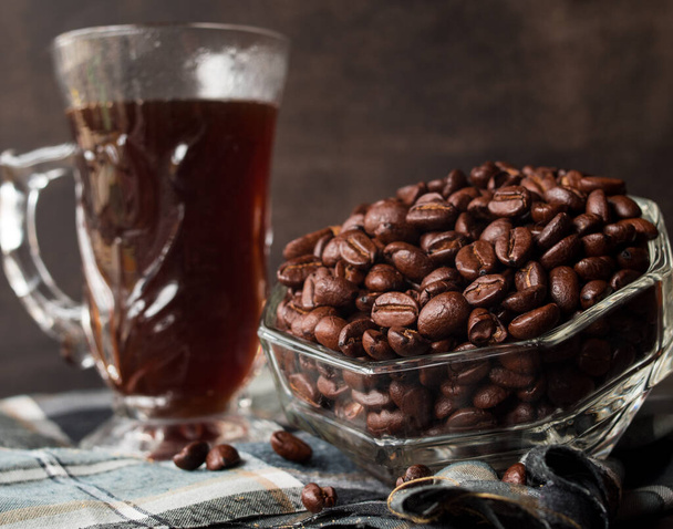 Algunos granos de café negro en una olla de vidrio junto a una taza de café negro - Foto, Imagen