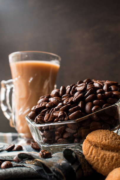 Niektóre czarne ziarna kawy w szklanym garnku obok filiżanki cappuccino i dzbanek mleka - Zdjęcie, obraz