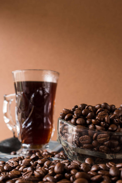 Μερικά μαύρα φασόλια καφέ σε μια γυάλινη κατσαρόλα δίπλα σε ένα φλιτζάνι μαύρο καφέ - Φωτογραφία, εικόνα