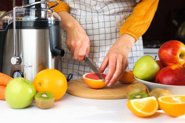 A young woman cuts an grapefruit on a wooden board in the kitchen for making fresh juice. Close-up. Selective focus. - Foto, Bild