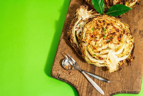 Homemade vegan cabbage steaks with herbs and spices. Healthy food ready to eat on a wooden cutting board. Modern hard light, dark shadow, bright green background, top view - Foto, Imagen
