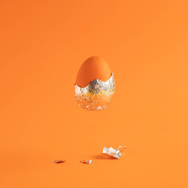 Creative Easter egg with foil against an orange background. Creative holiday or futuristic concept. - Photo, Image