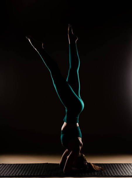 Silhueta de menina atraente e bonita está equilibrando em sua cabeça com as pernas para cima, enquanto se concentra na pose no estúdio - Foto, Imagem