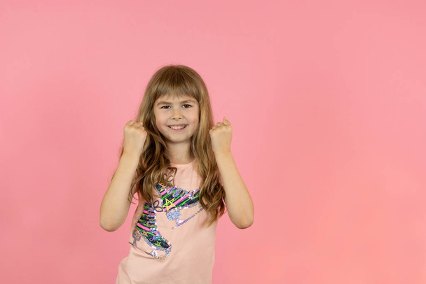 Niña posando alegremente sobre un fondo rosa. Una hermosa niña posa alegremente sobre un fondo de estudio rosa. Emociones infantiles para la publicidad.  - Foto, Imagen