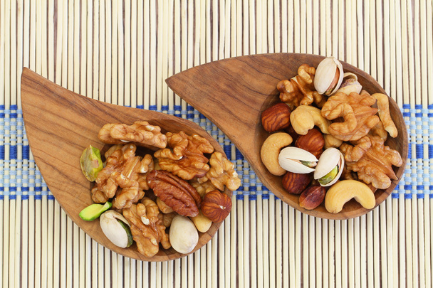 Selection of mixed nuts in wooden bowls on bamboo mat - Photo, Image