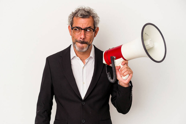 Middle age business man holding a megaphone isolated on white background  confused, feels doubtful and unsure. - Photo, image