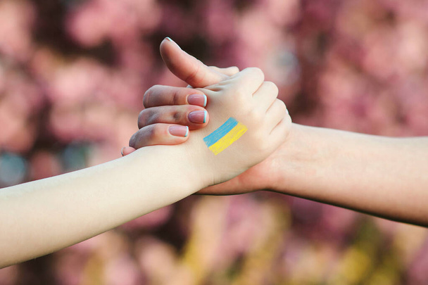 ウクライナ人の子供はボランティアの手を握っている。子供は手描きでウクライナ国旗の色を描いた。ウクライナを支援する。ウクライナの子供たちのサポート. - 写真・画像