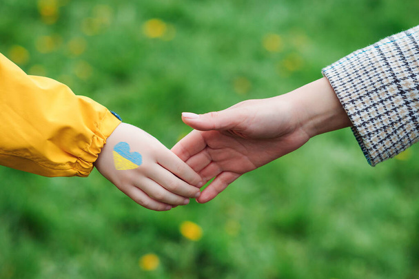 Bambino ucraino tiene la mano di un volontario. Il bambino dipinse a mano i colori della bandiera ucraina. Sostieni l'Ucraina. Sostegno ai bambini ucraini. - Foto, immagini