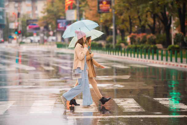 Beautiful and attractive girls are crossing the street together on the rain - Photo, Image