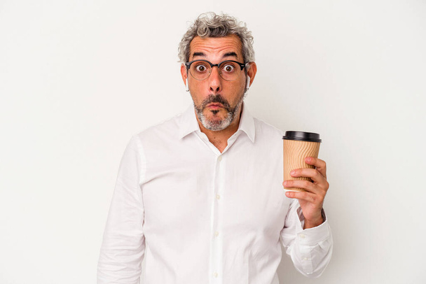 Geschäftsmann mittleren Alters, der einen Kaffee zum Mitnehmen auf weißem Hintergrund hält, zuckt mit den Schultern und öffnet verwirrt die Augen. - Foto, Bild