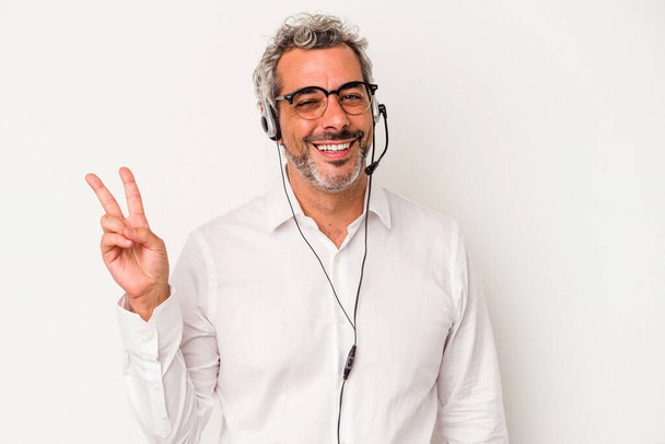 Homem caucasiano telemarketer de meia idade isolado em fundo branco alegre e despreocupado mostrando um símbolo de paz com os dedos. - Foto, Imagem