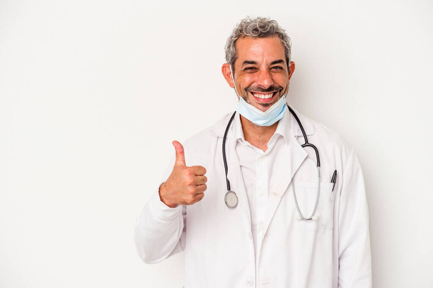 Middelbare leeftijd arts man met een masker voor virus geïsoleerd op witte achtergrond glimlachen en het verhogen van duim omhoog - Foto, afbeelding