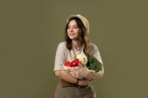Zero waste concept. Young brunette woman holding reusable cotton shopping mesh bag with organic groceries from a market. Concept of no plastic. Zero waste, plastic free. Sustainable lifestyle. - Photo, image