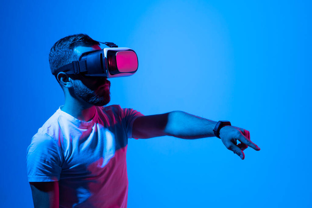 Portrait of man in black t-shirt wearing 3d headset glasses gesturing as if touching something what he doing in virtual reality while playing video games. Metaverse. - Photo, Image