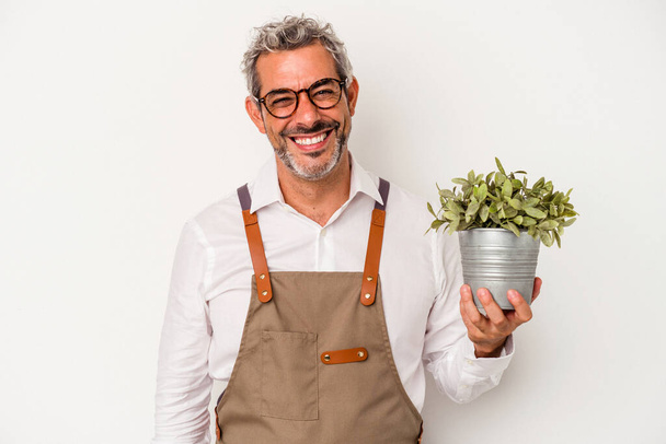 Μεσήλικας κηπουρός καυκάσιος που κρατάει ένα φυτό απομονωμένο σε λευκό φόντο χαρούμενος, χαμογελαστός και χαρούμενος. - Φωτογραφία, εικόνα