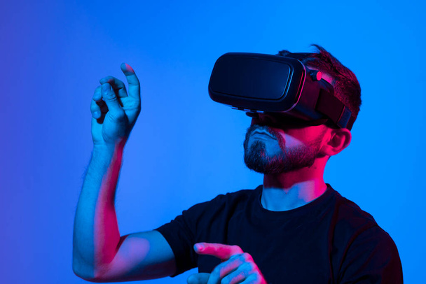 Man in virtual 3d glasses working on a project in a studio in neon light. Man playing video games with a friends at home using vr goggles. - Photo, Image